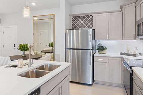 A modern kitchen with a stainless steel refrigerator and a large mirror above the sink at Parker Apartments in Raleigh, NC..