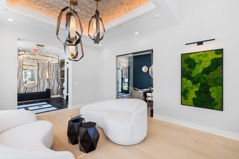 A modern sitting area with a white sofa, a black vase, and a green abstract painting on the wall at Parker Apartments in Raleigh, NC.