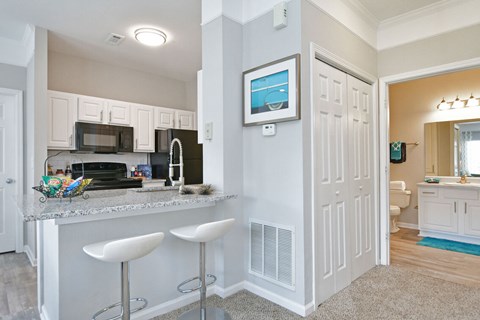 A kitchen with white cabinets and a white island with two stools.