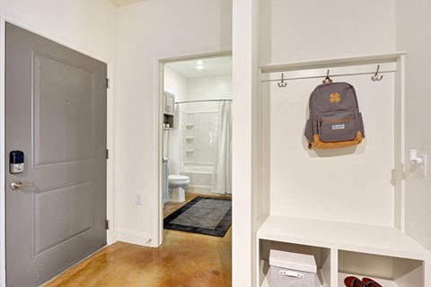 A backpack is hanging on a hook in a white hallway.