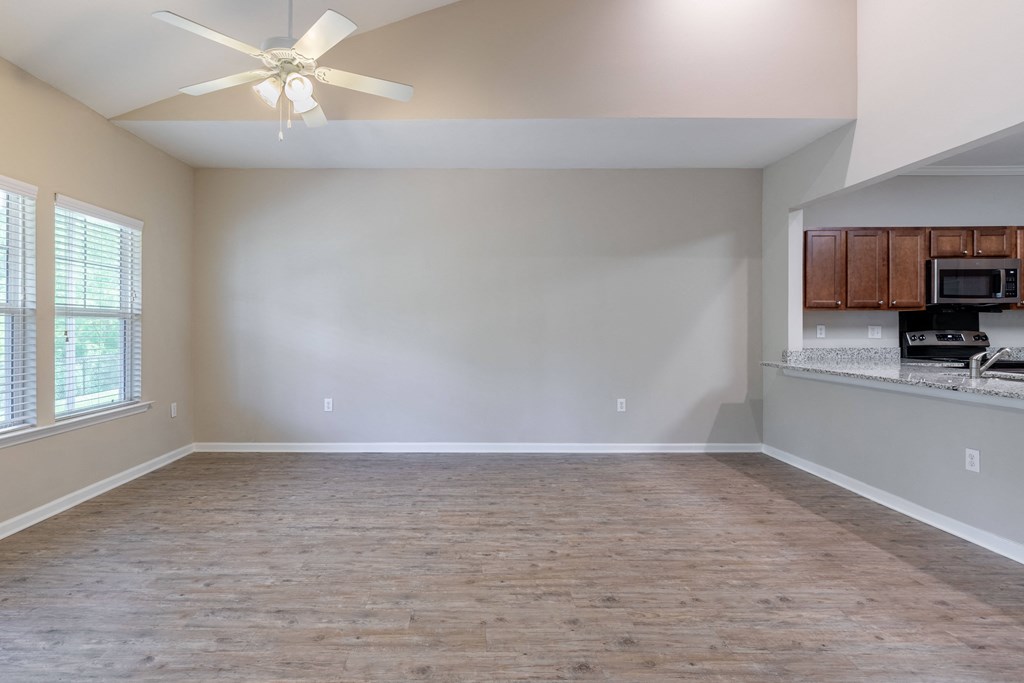 an empty living room with a kitchen and a ceiling fan