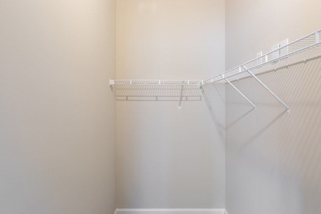 an empty walk in closet with white shelves and a white wall with a wire rack