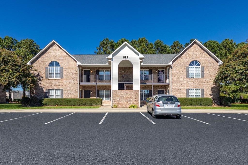 A silver car is parked in front of a two-story brick building.