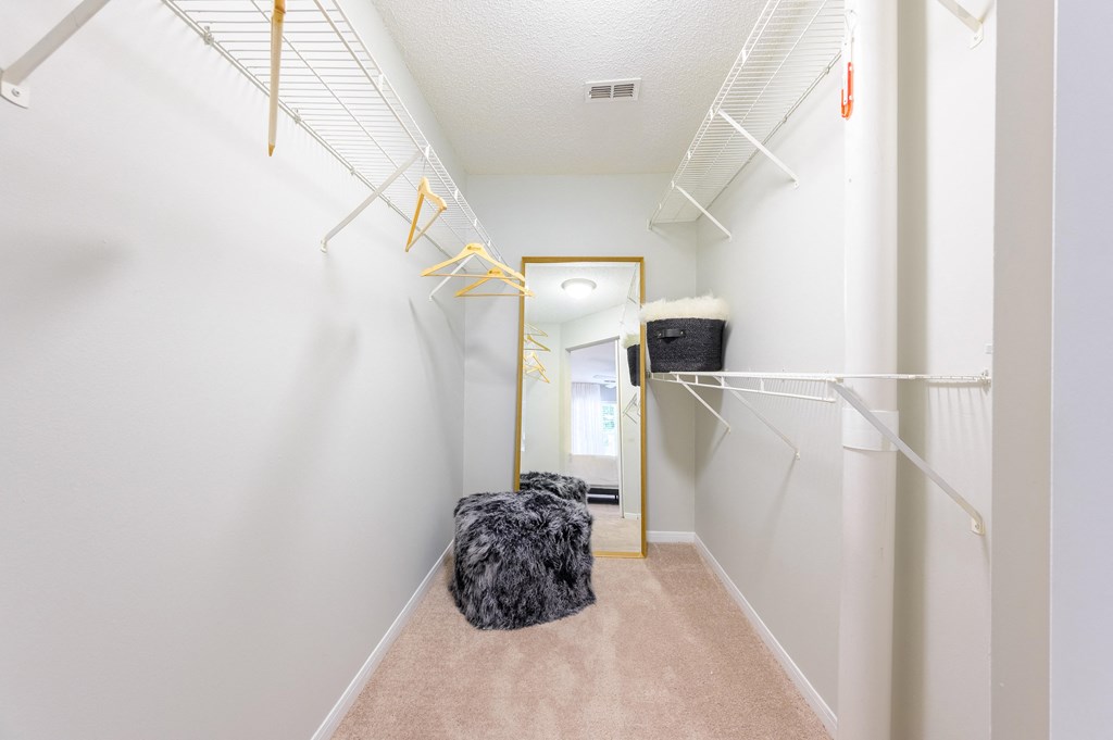 a walk in closet with white walls and a furry chair on the floor