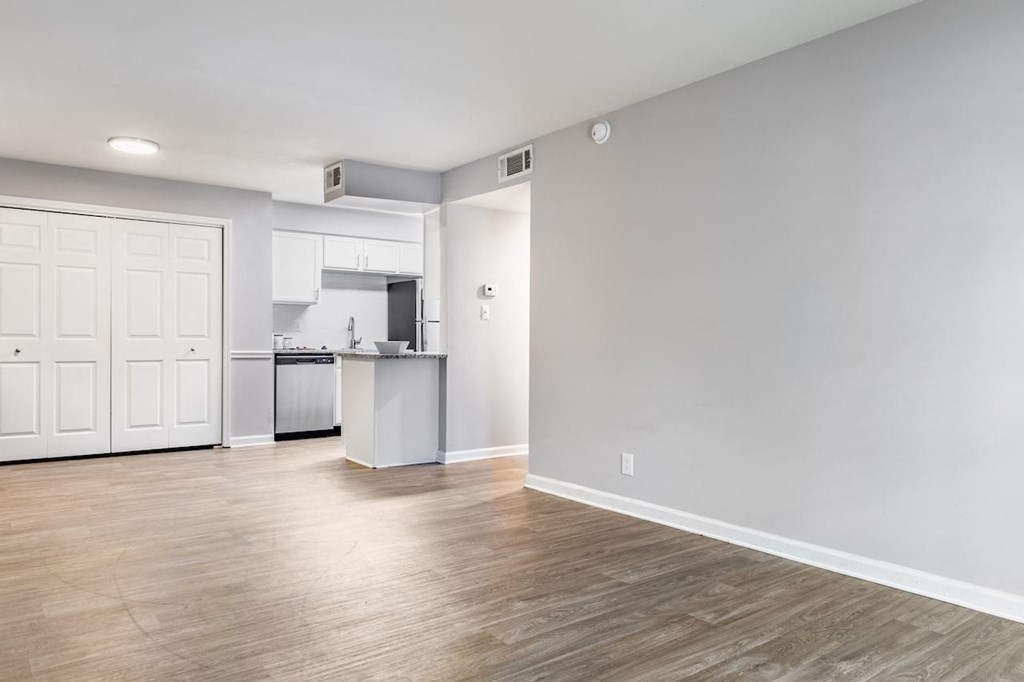 an empty living room with a kitchen in the background