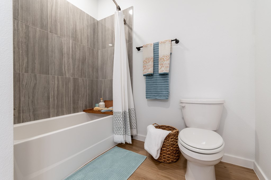 A bathroom with a toilet, a shower, and a basket on the floor.