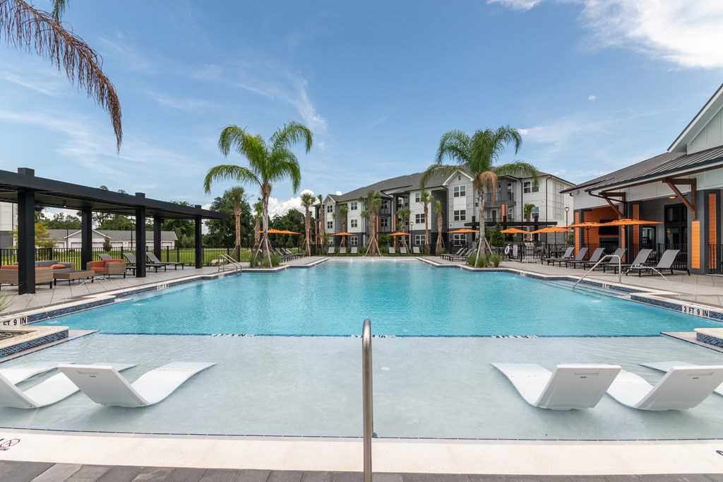 A large swimming pool with lounge chairs and a building in the background.