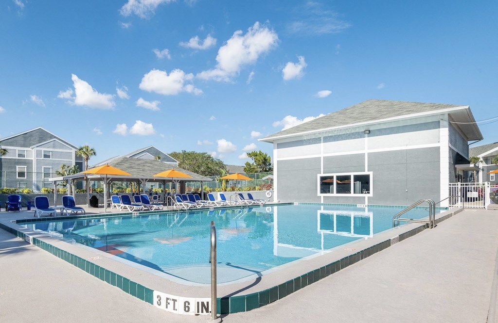 a large swimming pool with lounge chairs and umbrellas in front of a building