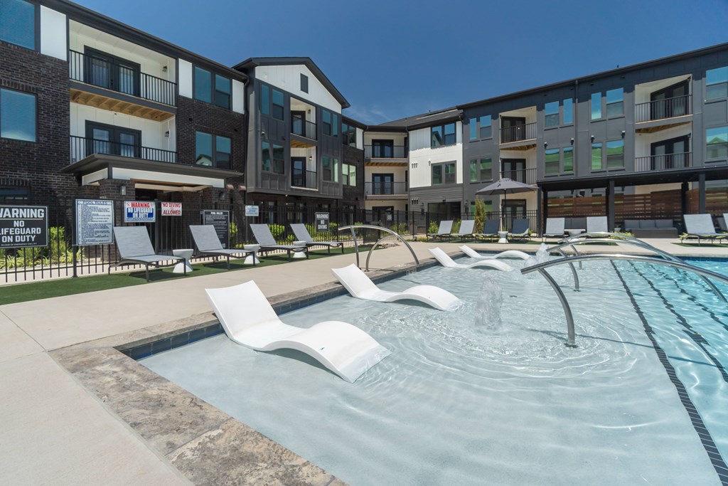 A pool area with white chairs and a warning sign in front of a building at Evolve Lake Norman apartments in Mooresville, NC