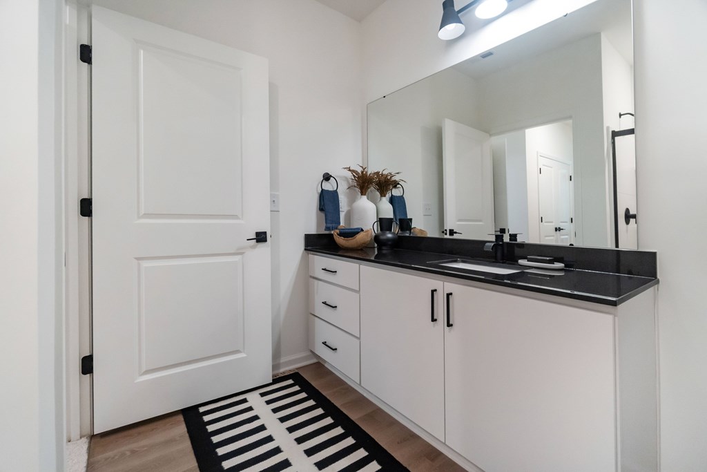 A bathroom with a white door, black countertop, and a striped rug at Evolve Lake Norman apartments in Mooresville, NC
