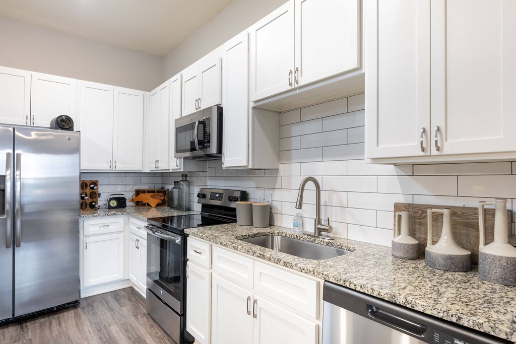 a kitchen with white cabinets and granite counter tops and stainless steel appliances
