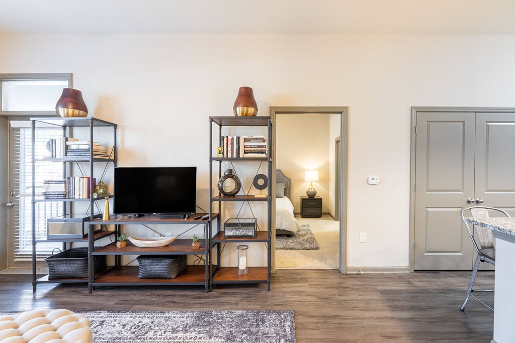 a living room with a television and shelving and a door to a bedroom