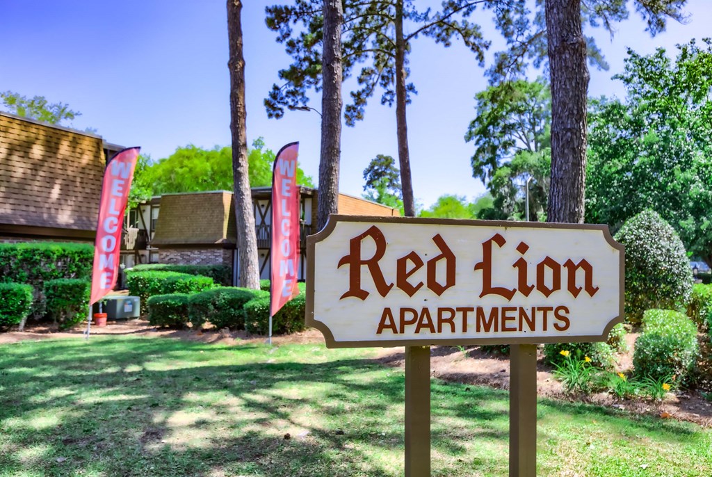 a red lion apartments sign in front of a yard with trees