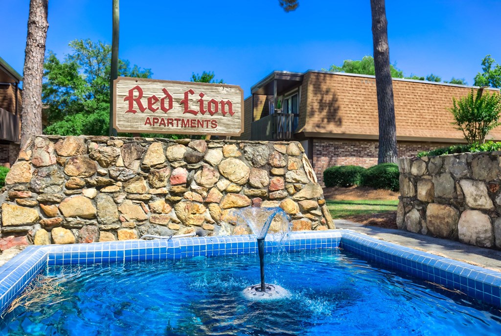 a pool with a fountain in front of the red lion apartments sign