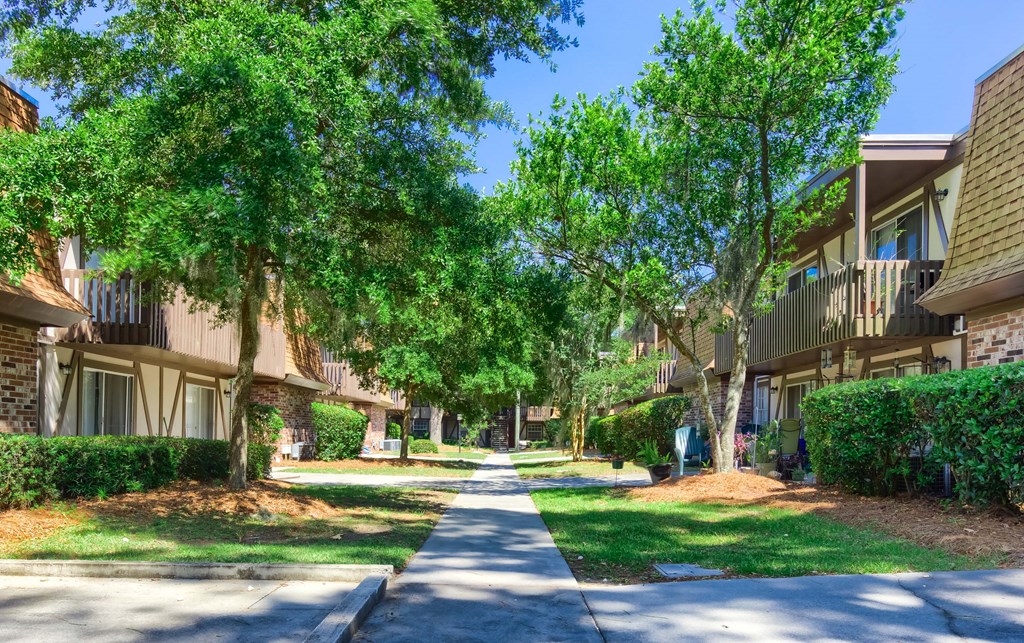 a sidewalk between two apartment buildings with green trees