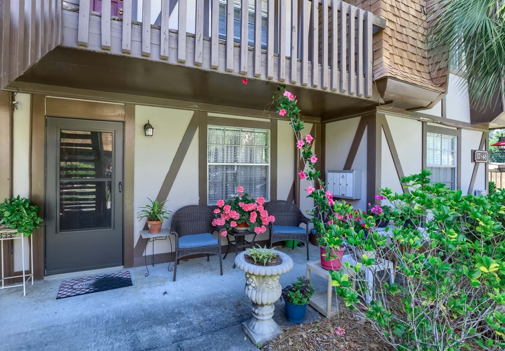 the front porch of a house with chairs and potted plants