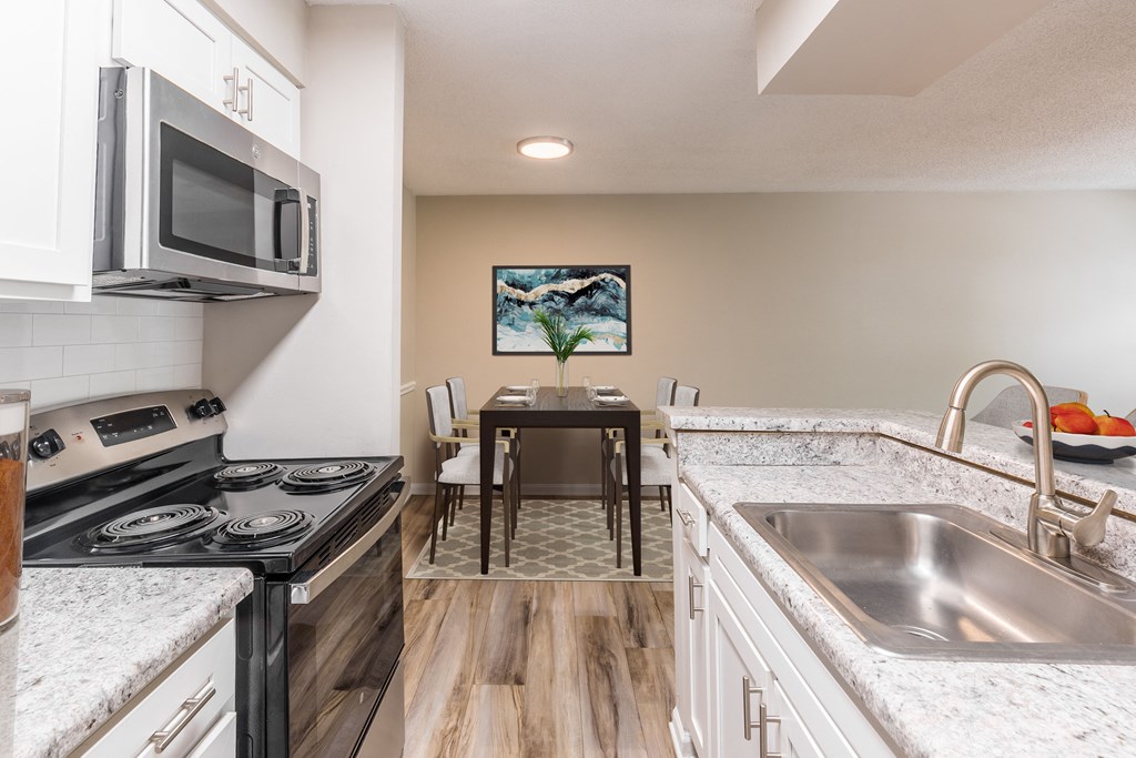a kitchen with white cabinets and granite countertops and a wooden dining room table with white chairs