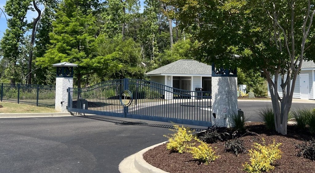 A gated entrance to a residential area with a house and trees.