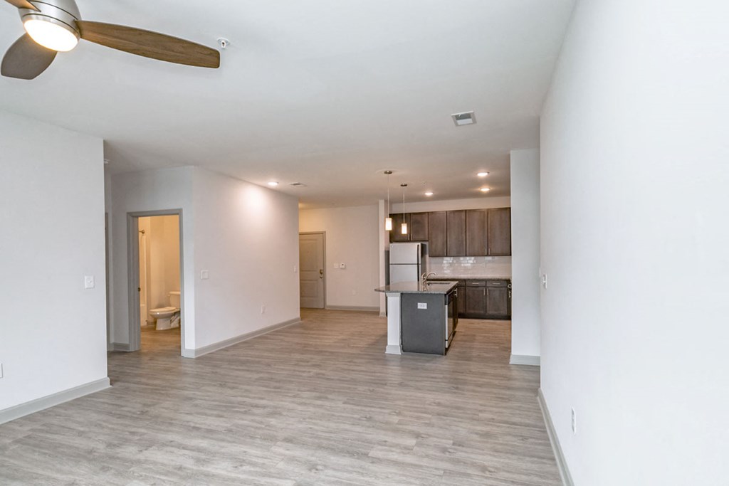 an empty living room with a kitchen and a ceiling fan