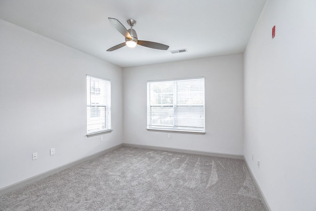 an empty living room with a ceiling fan and two windows