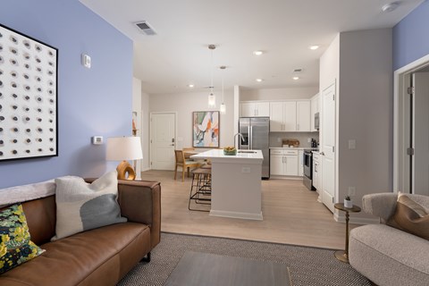 A modern living room with a brown leather couch and a kitchen in the background at Evolve Holly Ridge Apartments in Holly Ridge, NC.