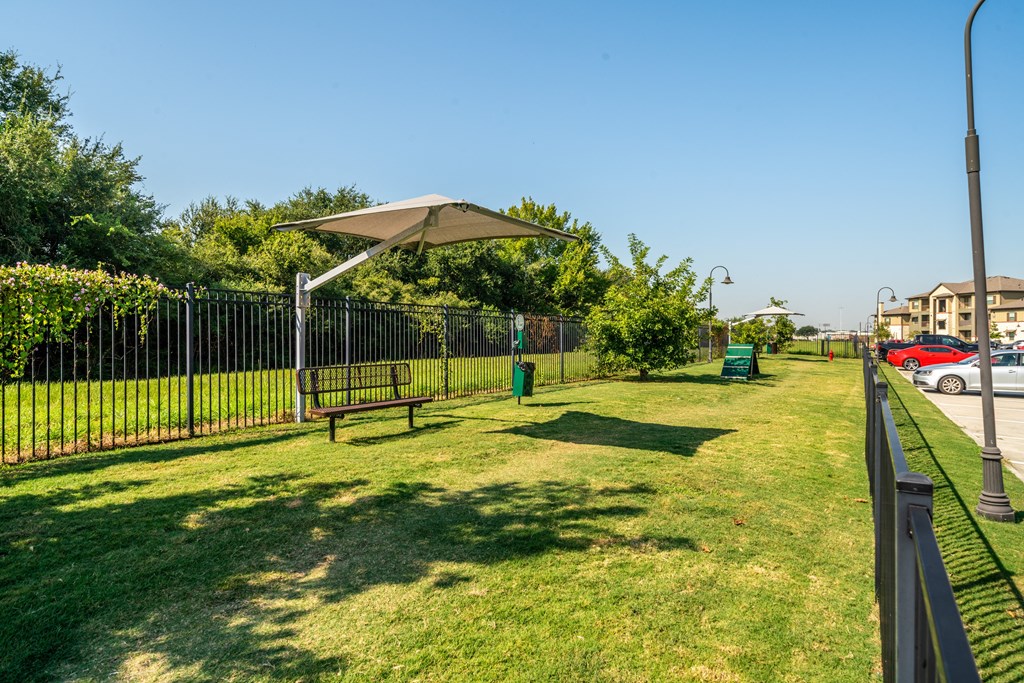 a park with a bench and an umbrella in front of a fence
