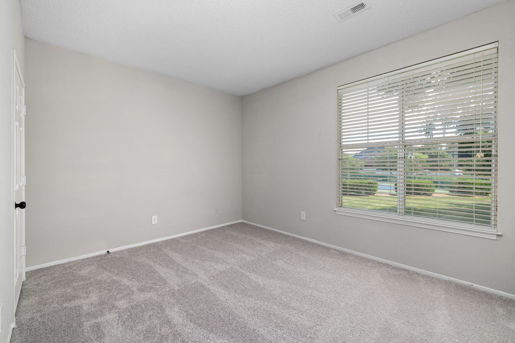 an empty bedroom with a large window and carpeting