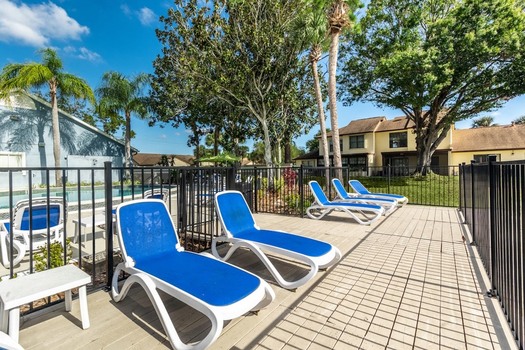 a patio with blue lounge chairs and a pool in the background