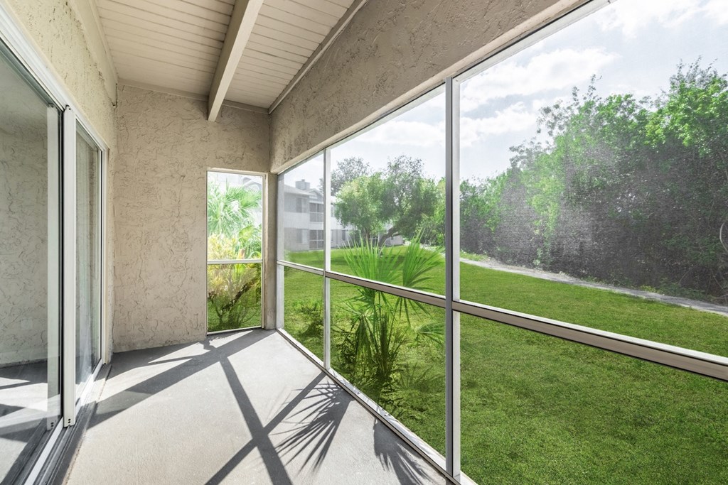 a screened in porch with a view of a grassy area and a building in the background