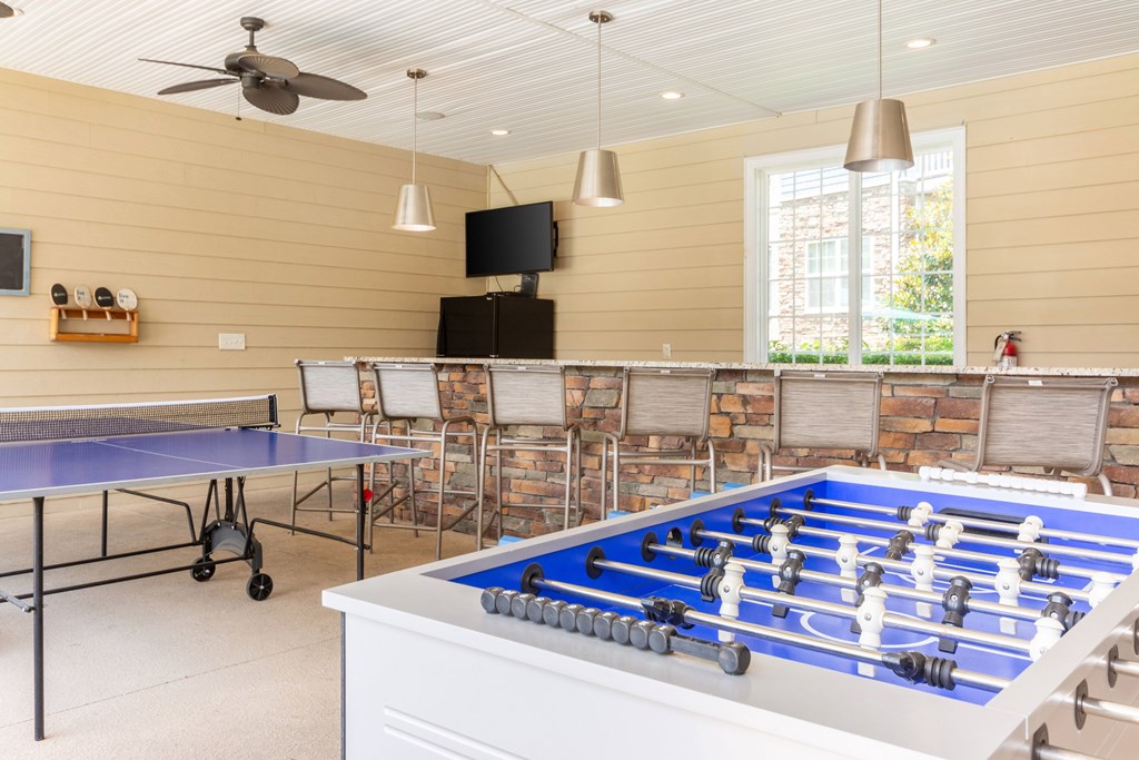 A foosball table is in the middle of a room with a ping pong table and chairs.