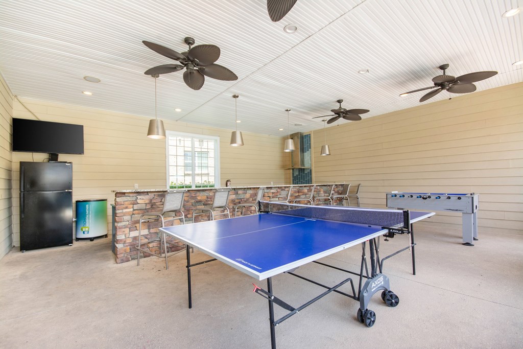 A blue ping pong table is in the middle of a room with a ceiling fan.