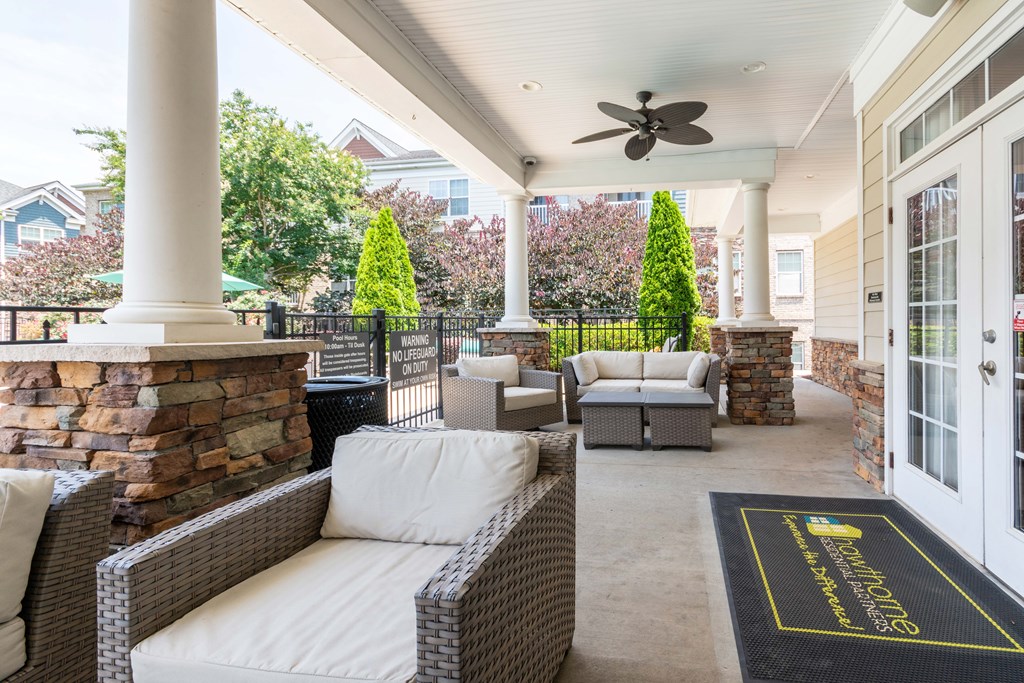 A patio with a wicker couch and a black mat that says