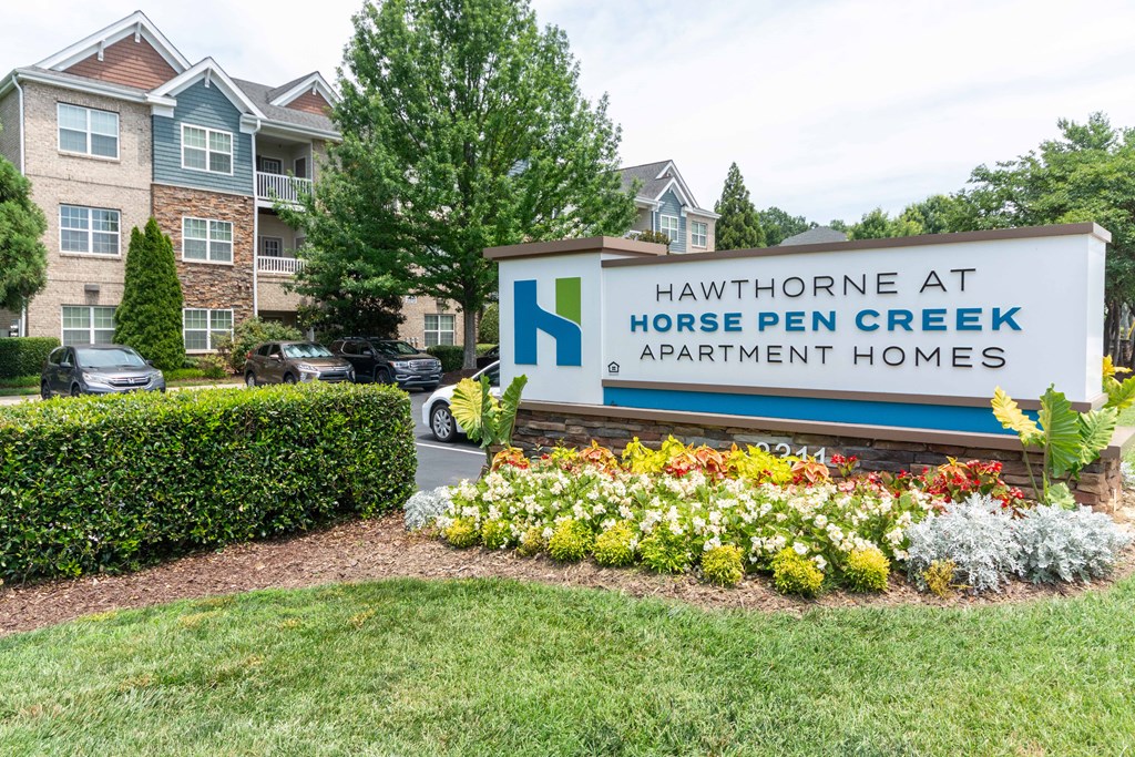 A sign for Hawthorne at Horse Pen Creek Apartment Homes is in front of a building.