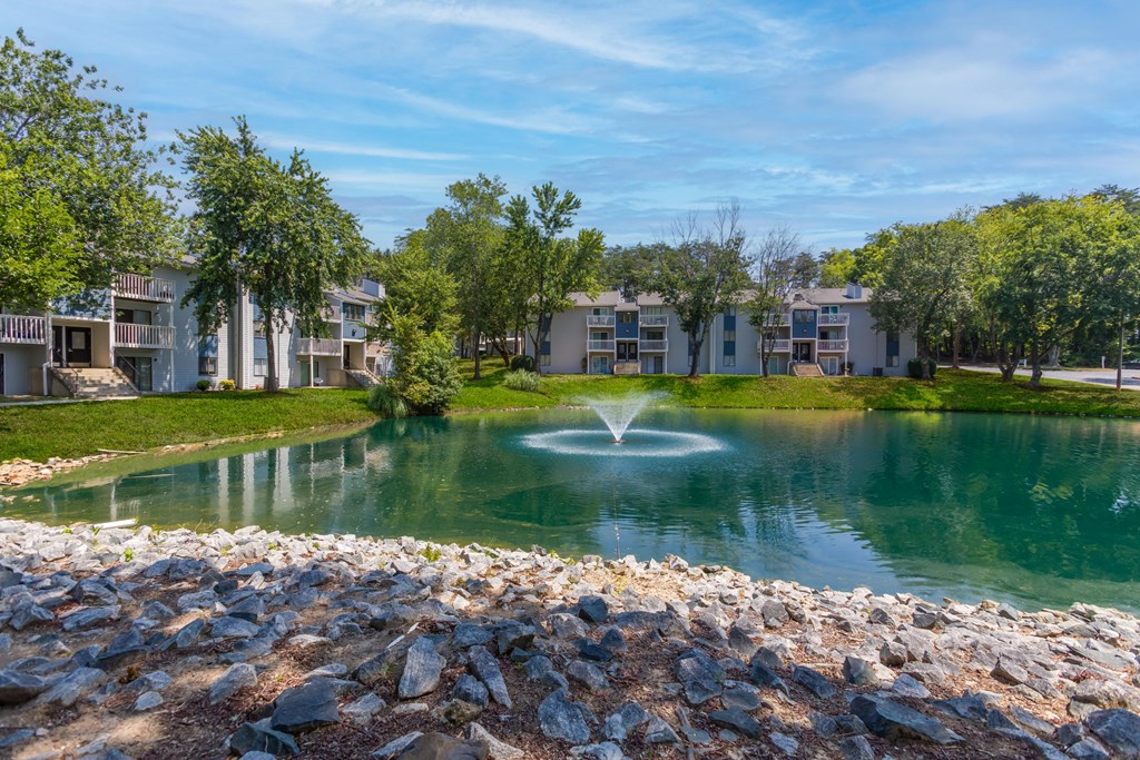 a fountain in the middle of a pond with apartments in the background
