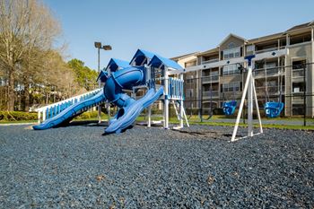 a playground with a blue slide and swing set in front of an apartment building