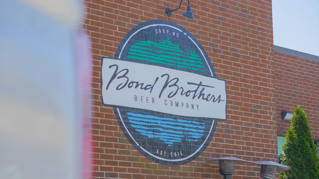 A sign for Bond Brothers Beer Company is mounted on a brick wall.
