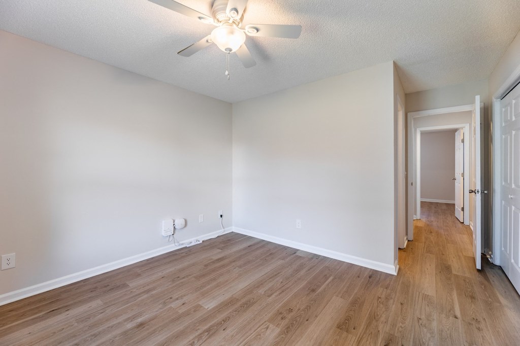 A room with a ceiling fan and light fixture, hardwood floors, and white walls.