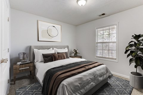 A bedroom with a bed, nightstand, and a plant.