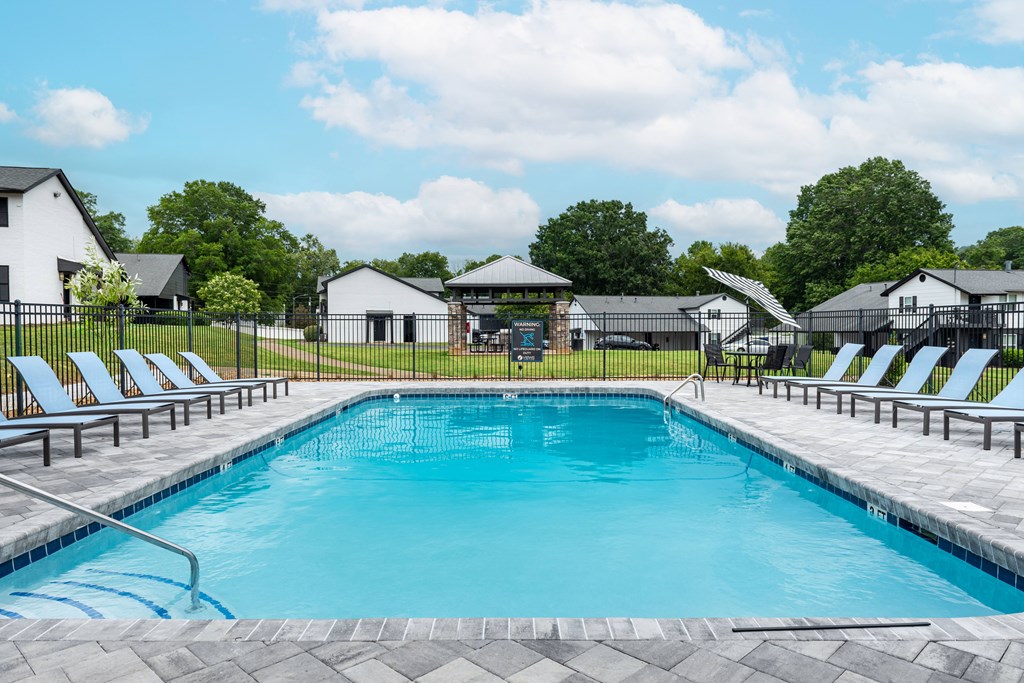 A swimming pool surrounded by lounge chairs and a fence.