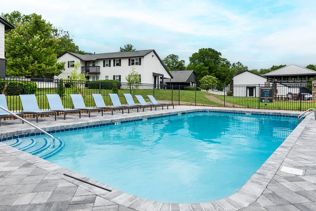 A large outdoor swimming pool with a black fence and sun loungers.