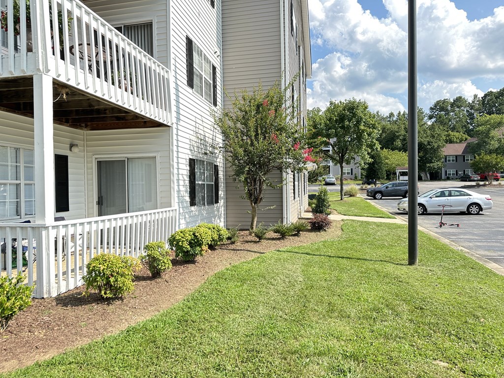 a white building with a porch and a lawn and bushes
