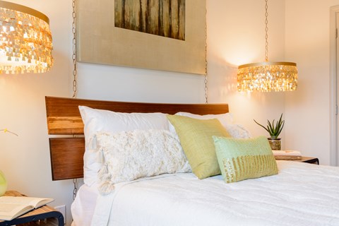 a bed with white sheets and pillows and two chandeliers