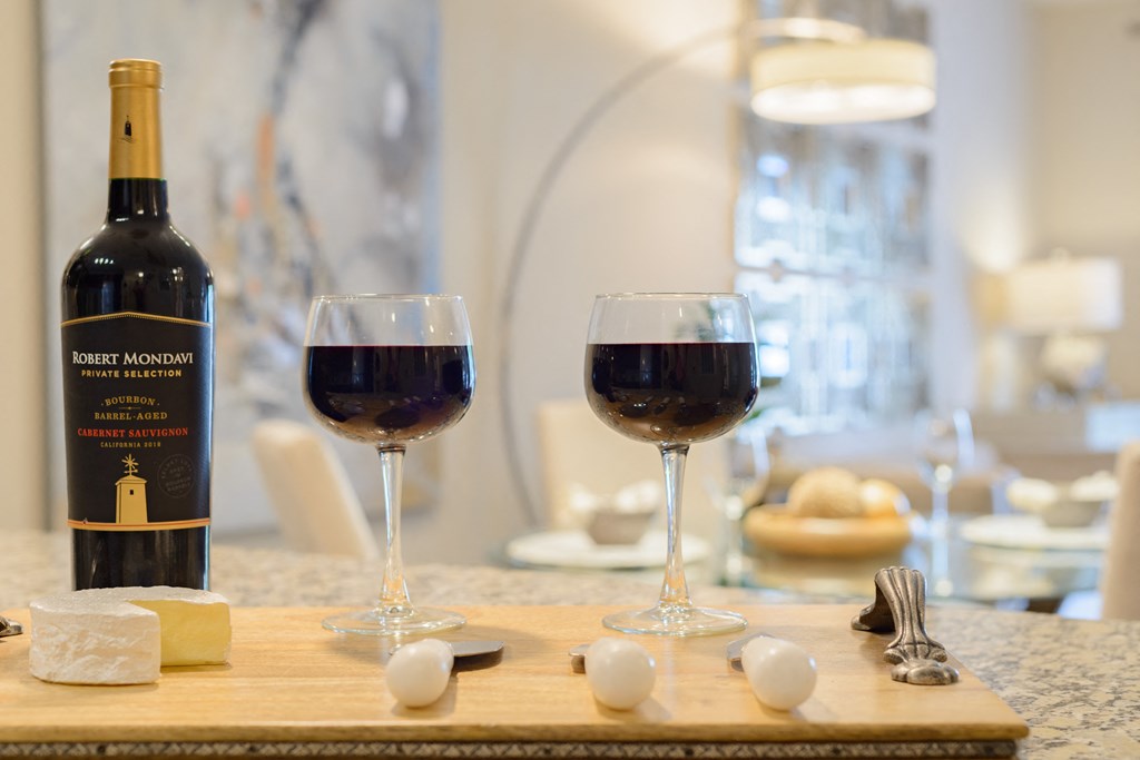two glasses of red wine next to a bottle of wine on a cutting board
