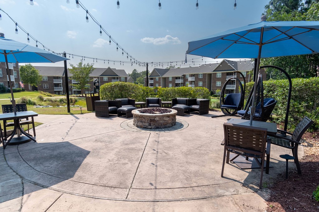a fire pit with umbrellas and chairs at the whispering winds apartments in pearland,