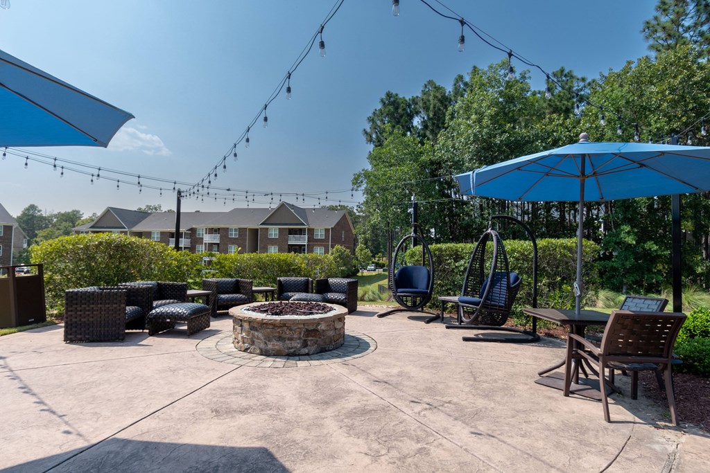 a firepit with chairs and umbrellas at the whispering winds apartments in pearland,