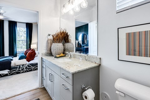 a bathroom with a vanity and a mirror and a bedroom with a bed