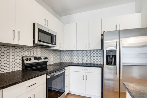 a kitchen with white cabinets and black counter tops and a stainless steel refrigerator