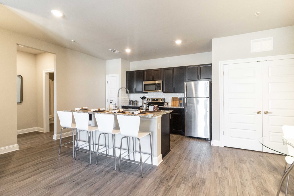 a kitchen with stainless steel appliances and a bar with white chairs