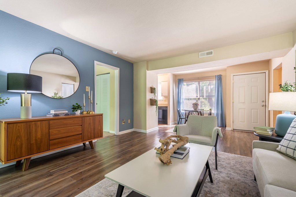 A living room with a white couch, a wooden dresser, and a round mirror at Hawthorne at Oak Ridge in Greensboro, NC.