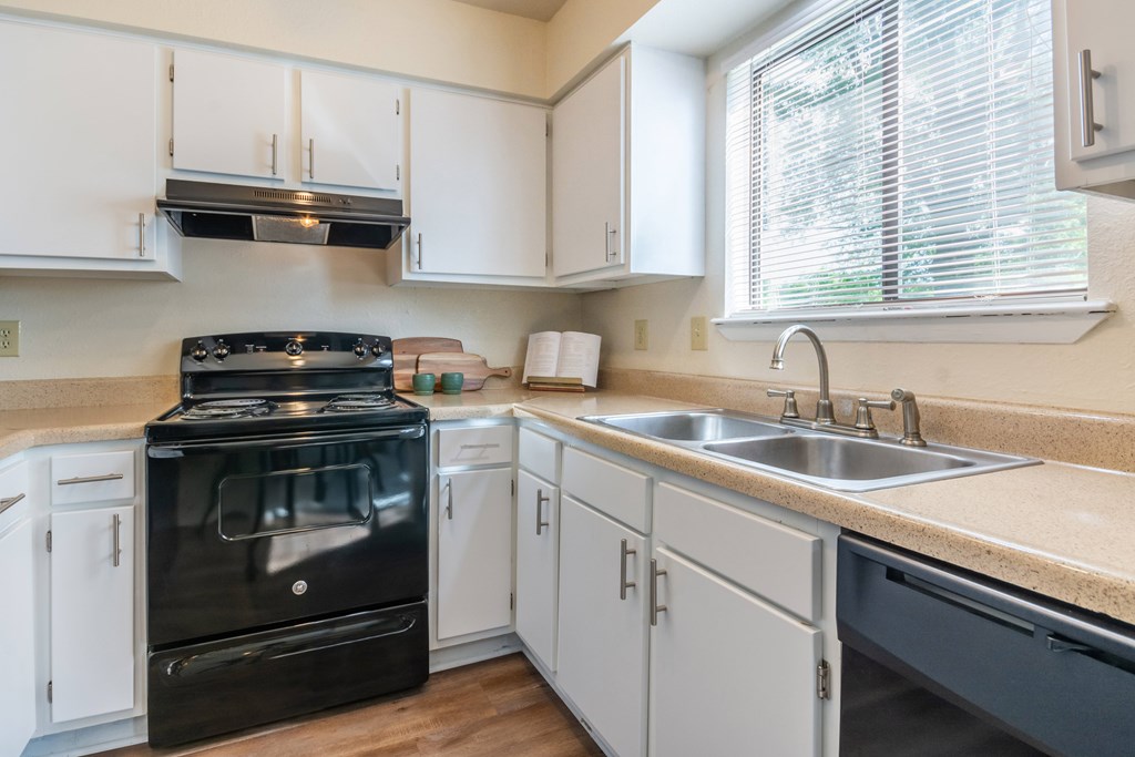 A black stove is in a kitchen with white cabinets at Hawthorne at Oak Ridge in Greensboro, NC.